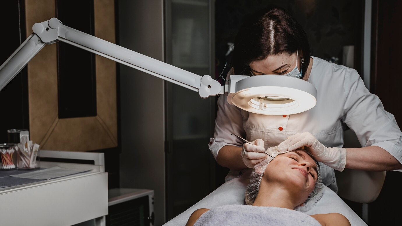 Profissional de estética atendendo uma cliente mulher deitada em uma mesa.